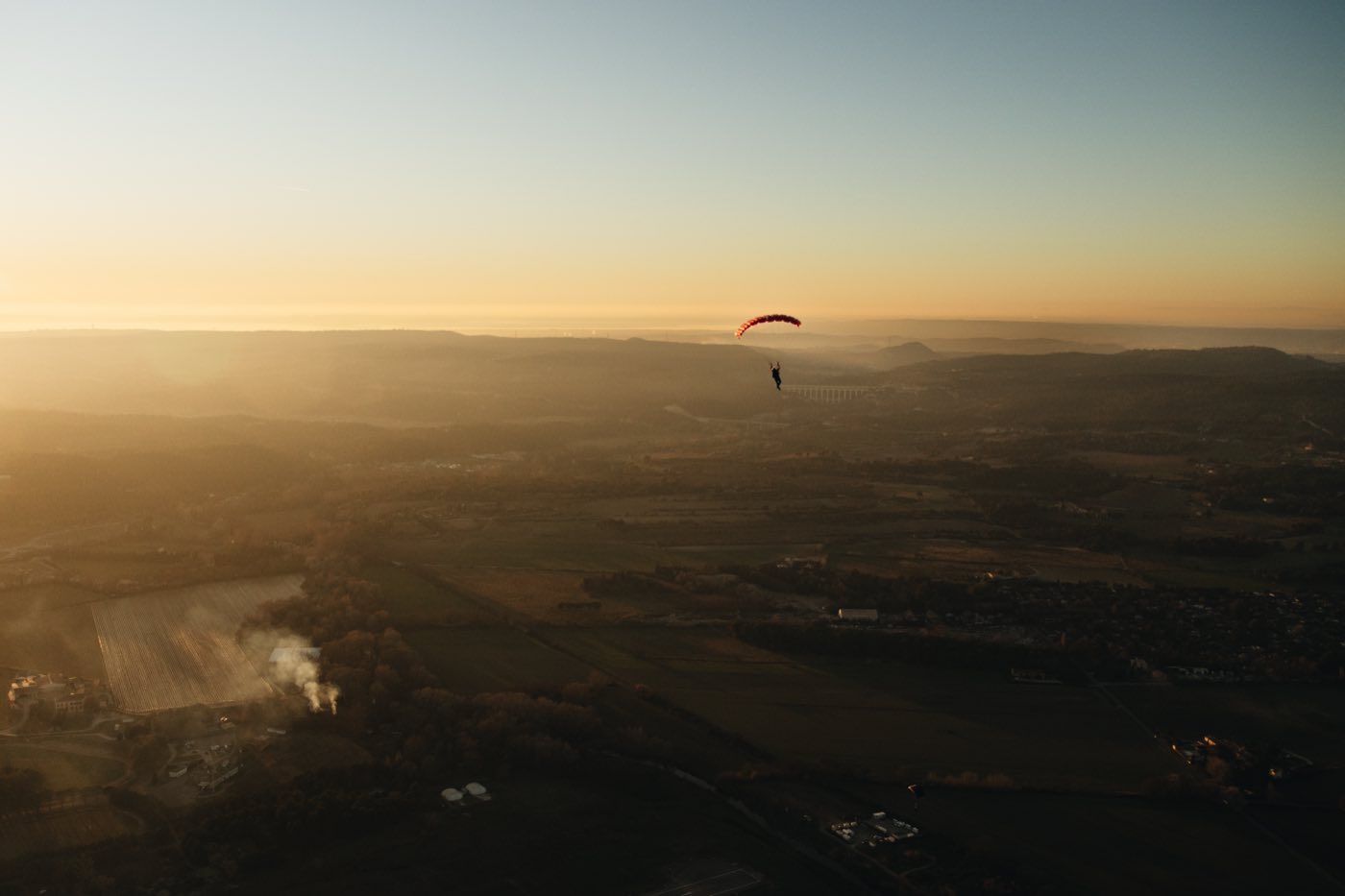 Un parachutiste sous voile au-dessus de la campagne au coucher du soleil